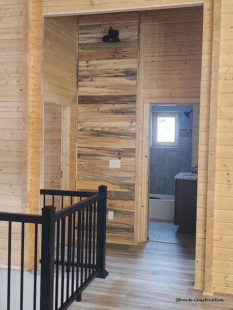 Log cabin upstairs landing with black metal railings, a beetle-kill pine accent wall, and a tiled bathroom beyond