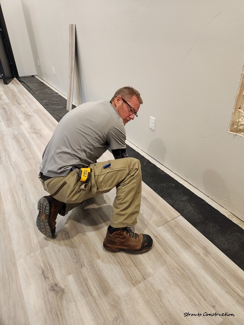 Master craftsman Chris Straub installing gray luxury vinyl plank flooring in a finished basement, Larimer County, Colorado