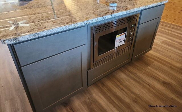 Gray shaker kitchen island with a granite countertop and built-in stainless microwave on luxury vinyl plank flooring
