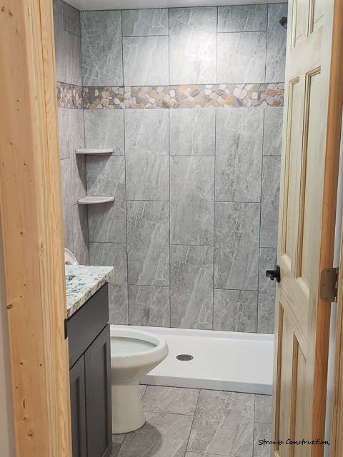 Remodeled bathroom with a gray marble-look tile tub surround, river-rock mosaic accent, and a granite-topped vanity