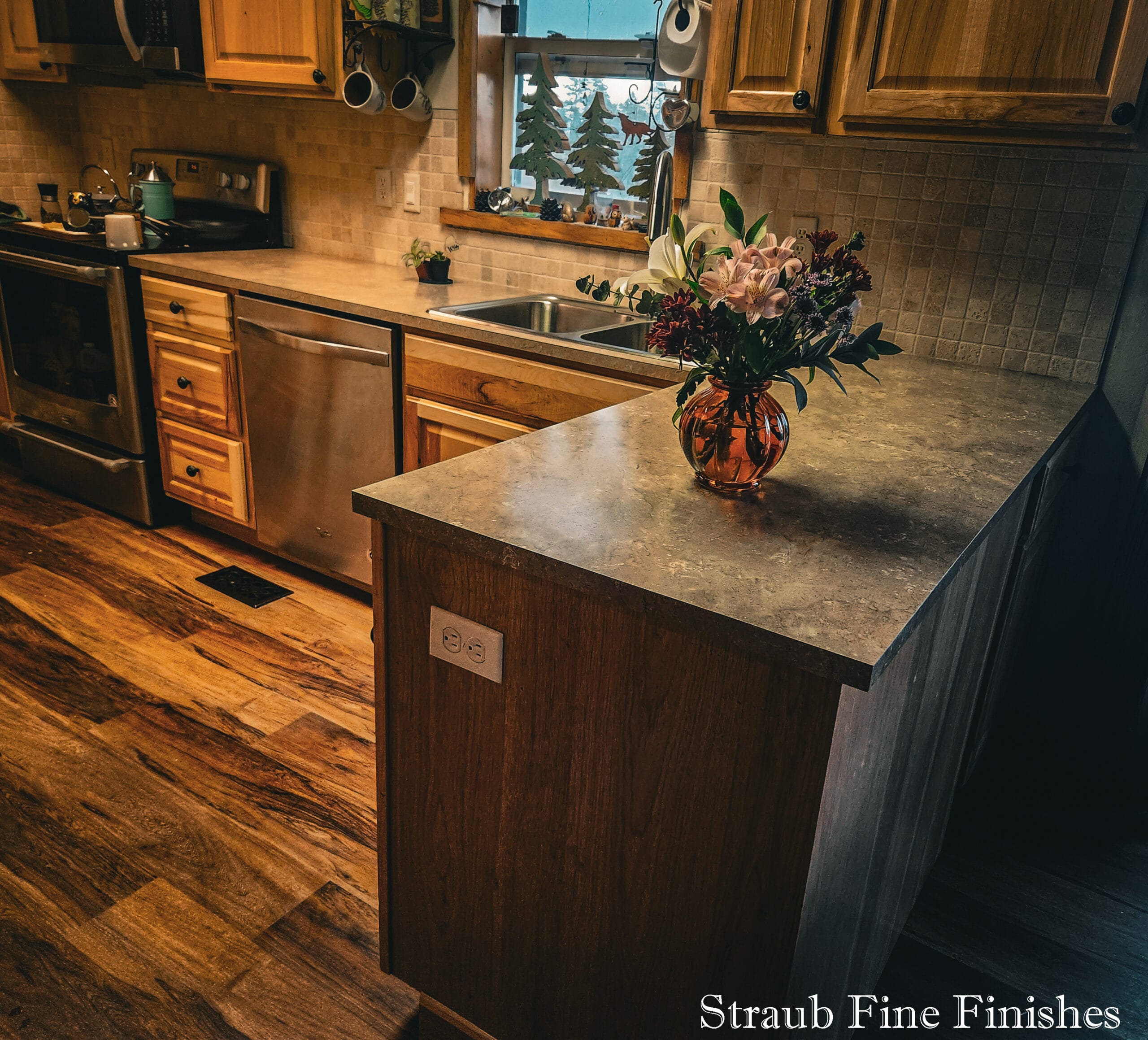 Updated 1897 cabin kitchen with honey-oak cabinets, stone-look counters, and a window over the sink framing the pines