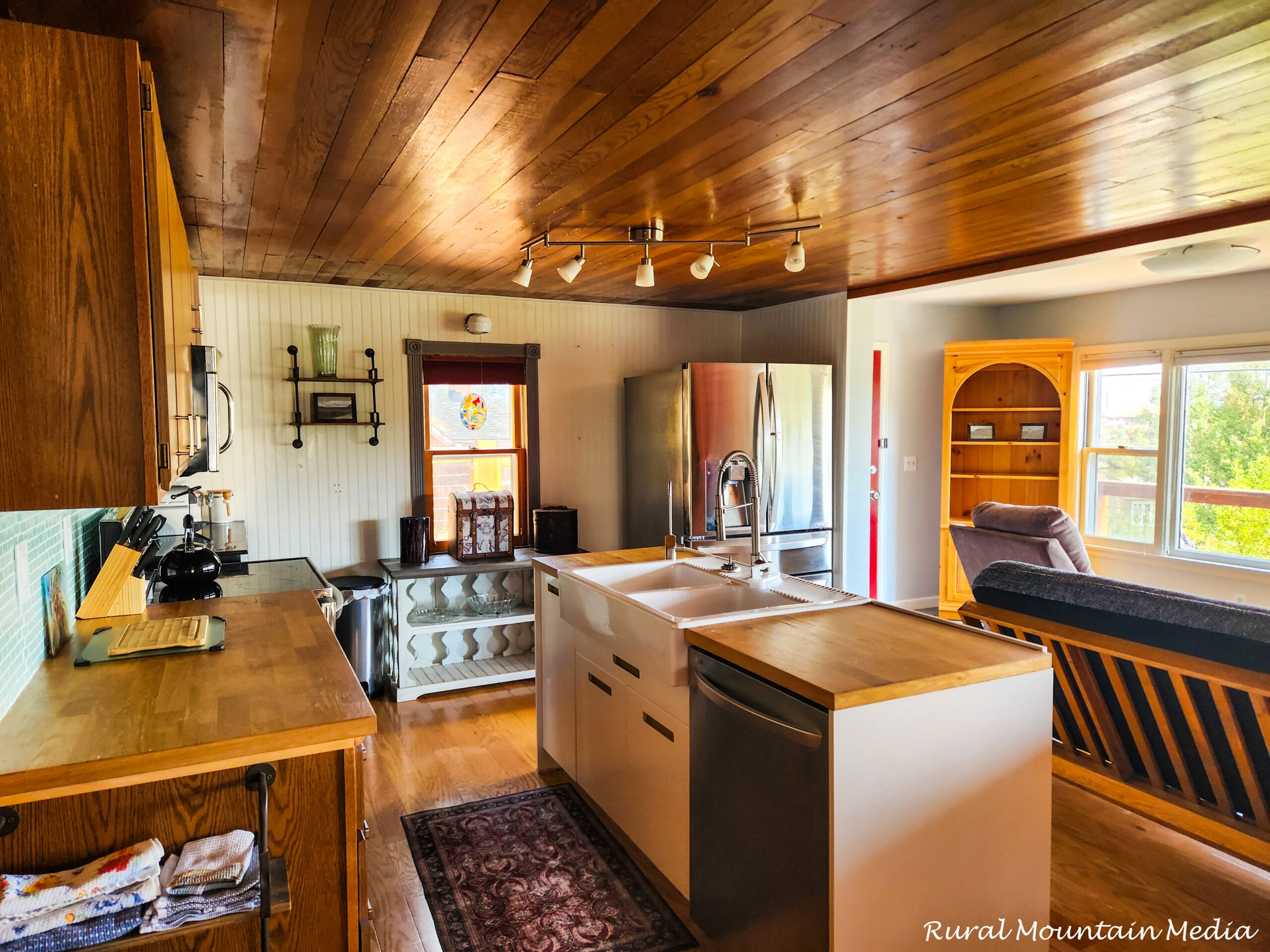 Open cabin kitchen with a knotty-pine ceiling, white island, and stainless appliances in a restored 1897 cabin